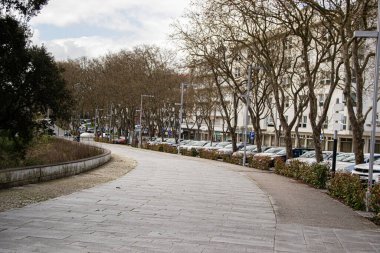 Fatima, Portekiz - 24 Mart 2025: Fatima, Portekiz 'de park halindeki araçlar ve yapraksız ağaçlarla kıvrımlı yürüyüş yolu