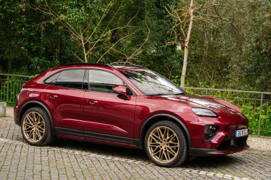 Fatima, Portekiz - 24 Mart 2025: Kırmızı SUV Porsche Macan arka planda yeşil ağaçlarla Fatima Portekiz 'de zarif bir şekilde park etmiş.