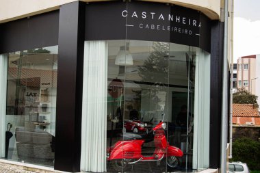 Fatima, Portekiz - 24 Mart 2025: Modern kuaför salonu Casta Nheira Cabeleireiro cam camlı iç mekan ve klasik Vespa kırmızı scooter Fatima.