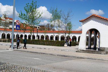 Fatima, Portekiz - 26 Mart 2025: Mimarlık, ağaçlar ve güneş ışığı altında yürüyen insanların yer aldığı Fatima 'da bir kasaba meydanı.