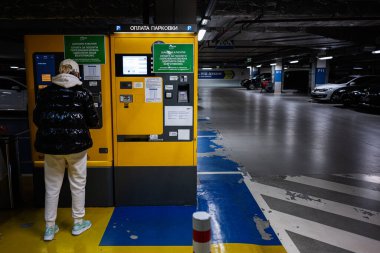 Lviv, Ukrayna - 31 Mart 2025: Parlak ışıklı bir otoparkta ödeme terminali işleten kişi