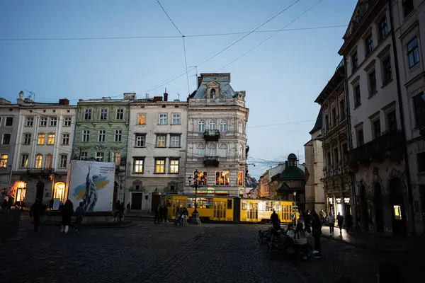Lviv, Ukrayna - 31 Mart 2025: Alacakaranlıkta sarı tramvaylı tarihi kaldırım taşı meydanı ve Ukrayna 'nın Lviv kentindeki eski binalar. 