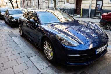 Lviv, Ukrayna - 01 Nisan 2025: Zarif mavi sedan Porsche Panamera 4 arabası Lviv, Ukrayna 'da bir kaldırım taşı caddesinde park edilmiş.