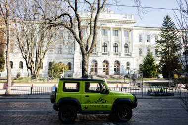 Lviv, Ukrayna - 1 Nisan 2025: Canlı yeşil bir Suzuki Jimny SUV Lviv 'de klasik bir binanın önüne park etmiş.