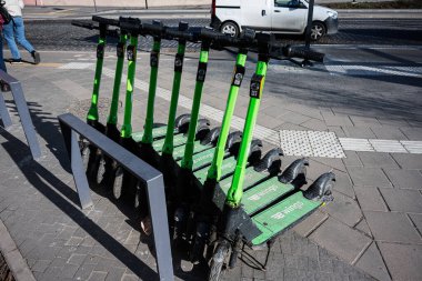 Lviv, Ukrayna - 1 Nisan 2025: Parlak yeşil elektrikli scooterlar güneşli bir kentsel caddedeki bir rıhtım istasyonunda hizalandılar. 