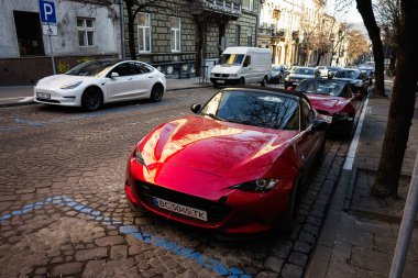 Lviv, Ukrayna - 01 Nisan 2025: Kırmızı bir spor araba Mazda MX-5 ve beyaz Tesla Lviv, Ukrayna 'da bir şehir caddesi boyunca park halindedir.
