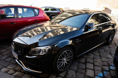 Lviv, Ukrayna - Nisan 01, 2025: Parlak siyah Mercedes-Benz C-Sınıfı araba modern tasarım ile kaldırımlı yol ve kentsel mimariye karşı fotoğraflandı