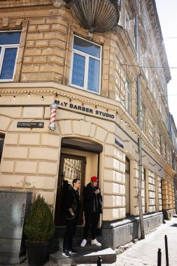 Lviv, Ukrayna - Nisan 06, 2025: Berber stüdyosunun önünde iki adam bulunan klasik bir binanın görüntüsü.