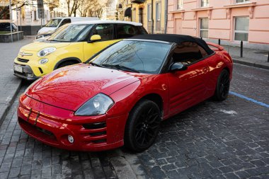 Lviv, Ukrayna - Nisan 06, 2025: Üstü açılabilir kırmızı Mitsubishi Eclipse arabası sarı bir aracın yanında kaldırım taşı bir caddeye park edilmiş. 