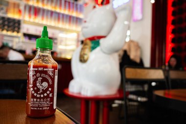Lviv, Ukrayna - Nisan 06, 2025: Sıcak Sriracha sosu şişesi masada bulanık restoran arkaplanı ve beyaz figürlü
