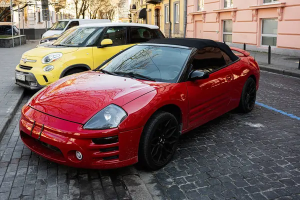 Lviv, Ukrayna - Nisan 06, 2025: Üstü açılabilir kırmızı Mitsubishi Eclipse arabası sarı bir aracın yanında kaldırım taşı bir caddeye park edilmiş. 