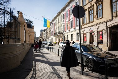 Lviv, Ukrayna - Nisan 06, 2025: Lviv 'de mimari, bayrak, yayalar ve park halindeki arabaları gösteren manzaralı bir sokak.