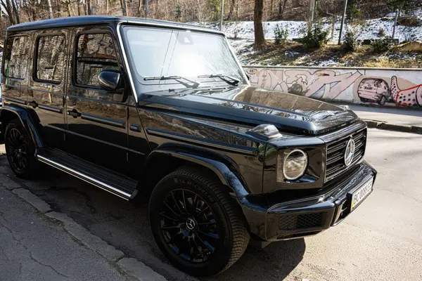Lviv, Ukrayna - Nisan 06, 2025: Lüks siyah Mercedes-Benz G 63 AMG SUV kentsel çevre ve graffiti ile sakin bir caddeye park edilmiş.