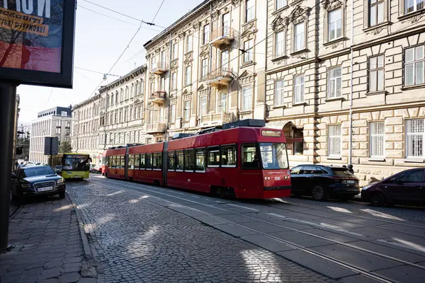 Lviv, Ukrayna - Nisan 06, 2025: Lviv, Ukrayna 'da klasik binalarla çevrili bir kaldırım taşından geçen kırmızı tramvay.