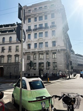 Milan, İtalya - 26 Mart 2025: Güneşli bir günde Microlino arabasının ve Milano 'daki tarihi binanın manzarası.