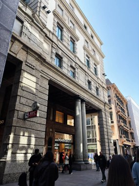 Milan, İtalya - 26 Mart 2025: Mimari ayrıntıları ön plana çıkaran taş cephesi, İtalya 'nın Milano kentindeki dükkanların yakınındaki insanlarla