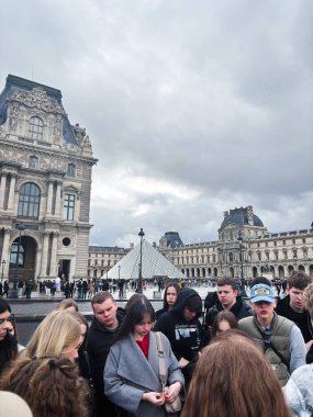 Paris, Fransa - 28 Mart 2025: Bulutlu bir gökyüzü ile Louvre Piramidi yakınlarında bir grup toplandı.