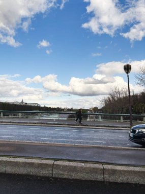 Paris, Fransa - 28 Mart 2025: Mavi gökyüzü, bulutlar ve uzaktan görülebilen şehir simgeleriyle şehir köprüsü manzarası. Paris, Fransa