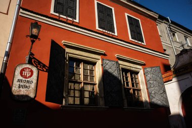 Lviv, Ukrayna - 07 Nisan 2025: Kırmızı cephe, güneşli pencereler ve sanatsal siyah panjurlar içeren sevimli Mons Pius mimarisi.