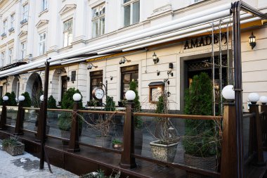 Lviv, Ukrayna - 07 Nisan 2025: Yeşillik ve eşsiz saat dekorasyonu ile Amadeus restoranının şık açık hava koltukları.