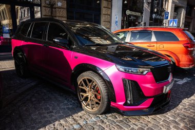 Lviv, Ukrayna - 07 Nisan 2025: Lviv 'de kaldırımda altın tekerlekleri olan modern pembe bir Cadillac XT6 SUV