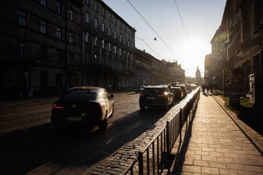 Lviv, Ukrayna - 07 Nisan 2025 Lviv, Ukrayna 'da gün batımıyla aydınlanan kaldırım taşı caddesindeki araçlar