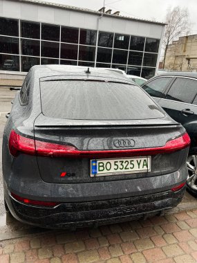 Kyiv, Ukrayna - 08 Nisan 2025: Koyu gri, modern bir Audi e-tron araba yağmurlu havada bir şehir caddesinde park halinde.. 