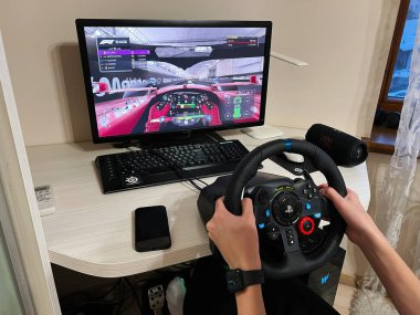 Kyiv, Ukrayna - 08 Nisan 2025: Evdeki monitörde F1 yarış simülatörü oynamak için direksiyon kullanan oyun meraklısı 