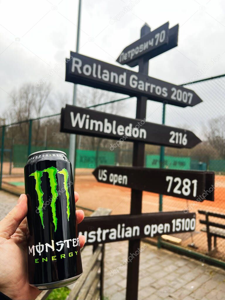Kyiv, Ukraine - April 08, 2025: Energy drink Monster can against signboard showing various sports destinations on tennis court.