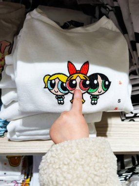 Kyiv, Ukrayna - 08 Nisan 2025: Powerpuff Girls tişörtüne dokunan çocuk eli bir mağaza vitrininde çizgi film karakterlerinin yer aldığı