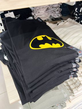 Kyiv, Ukrayna - 08 Nisan 2025: Simgesel Batman logosu ahşap raflarda düzgünce düzenlenmiş siyah tişört yığını.