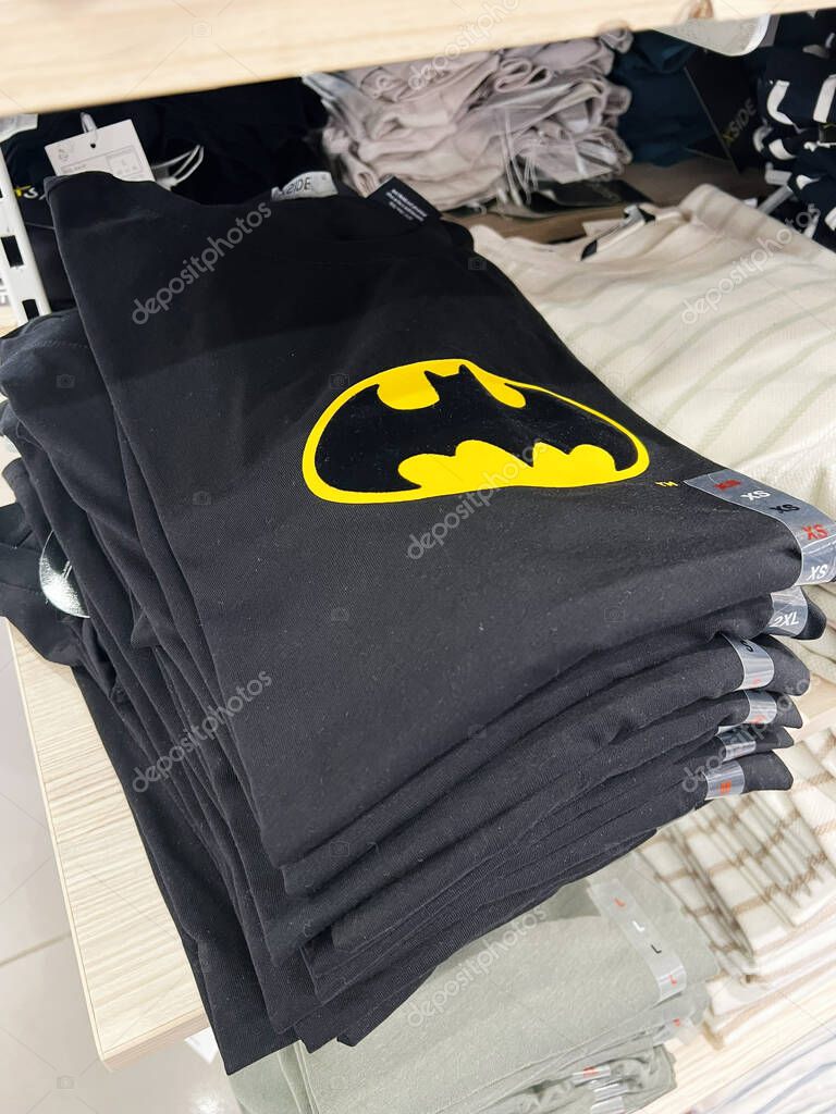 Kyiv, Ukraine - April 08, 2025: Pile of black t-shirts with iconic Batman logo arranged neatly on wooden shelves.