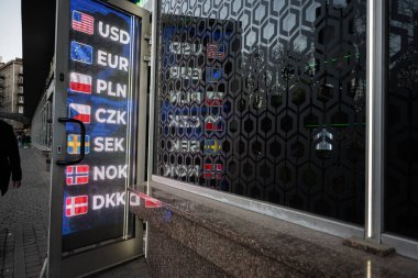 Bir finans merkezi girişinin dışında aydınlatılmış bir panoda para birimi oranları
