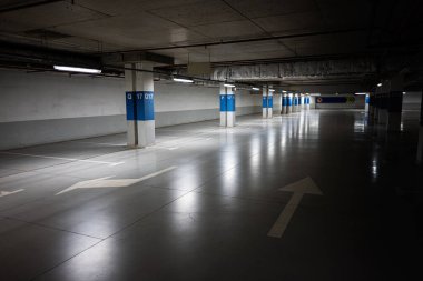 Yansıtıcı ışıklandırması ve yön gösteren okları olan geniş yeraltı otoparkı