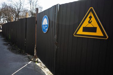 İnşaat alanının çitlerinde güvenlik gereksinimleri ve tehlikeleri gösteren uyarı levhaları.