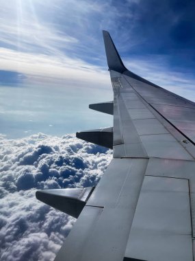 Bulutların üzerinde güneş ışığı ve mavi gökyüzü olan bir uçağın kanadı..