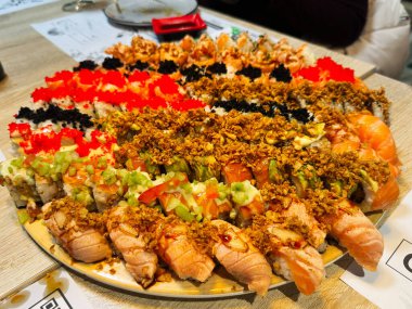 Ahşap bir masa üzerinde çeşitli malzemeler ve dolgularla canlı suşi ruloları.