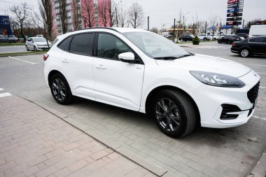Khmelnytskyi, Ukrayna - 16 Nisan 2025: Bulutlu bir gökyüzünün altında şehir manzarasıyla çevrili beyaz Ford Puma SUV.