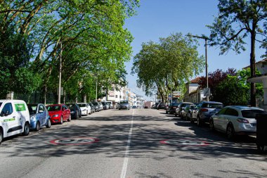 Caldas da Rainha, Portekiz - 17 Nisan 2025: Ağaçlar, park edilmiş arabalar ve güneşli hava ile Caldas da Rainha kentsel caddesi.
