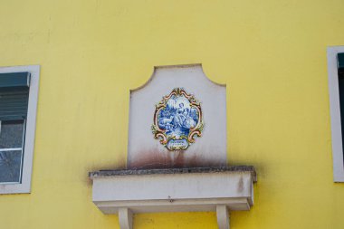 Caldas da Rainha, Portekiz - 17 Nisan 2025: Gölgeler tarafından vurgulanan canlı sarı bir duvar üzerinde klasik resimli dekoratif fayans.