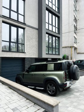 Kyiv, Ukrayna - 23 Nisan 2025: Green Land Rover Defender SUV kaldırımlı garaj yolundaki çağdaş bir konut binasının yanına park etti