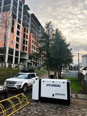 Kyiv, Ukrayna - 23 Nisan 2025: Jeneratör Hyundai inşaat halindeki bir binanın yakınındaki ağaçların ve kaldırımların arasında.