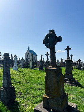 Khorostkiv, Ukrayna - 23 Nisan 2025: Tarihi mezarların ve güneş ışığı altında zarif bir şapelin yer aldığı huzurlu bir mezarlık sahnesi.