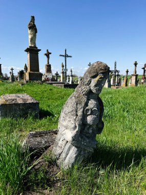 Khorostkiv, Ukrayna - 23 Nisan 2025: Çimenli bir arazide yıpranmış mezarların ve heykellerin yer aldığı sakin bir mezarlık sahnesi