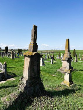 Khorostkiv, Ukrayna - 23 Nisan 2025: Mavi gökyüzünün altında eski mezar işaretleri ve canlı yeşil çimlerin yer aldığı sakin bir mezarlık