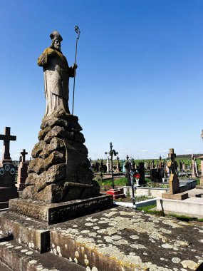 Khorostkiv, Ukrayna - 23 Nisan 2025: Huzurlu bir mezarlıkta mezartaşları ve haçları olan bir aziz heykeli.