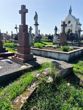 Khorostkiv, Ukrayna - 23 Nisan 2025: Mezarlık sahnesi mezar taşları, yeşil çimenler ve güneş ışığında bir kilise binası