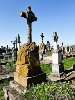 Khorostkiv, Ukrayna - 23 Nisan 2025: Eski bir mezarlık güneş ışığı altında yıpranmış mezar taşları, haçlar ve canlı yeşil çevreler içerir