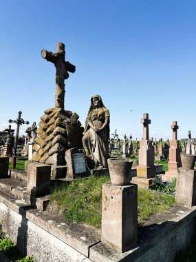 Khorostkiv, Ukrayna - 23 Nisan 2025: Çimenli bir manzaranın ortasında taş heykeller ve mezarcıların yer aldığı tarihi mezarlık