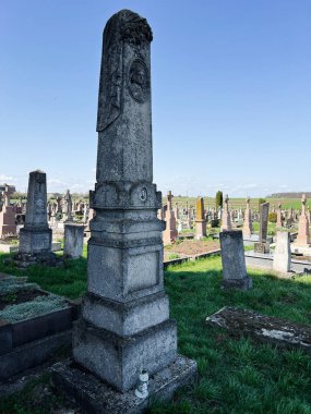 Khorostkiv, Ukrayna - 23 Nisan 2025: Çimenler ve diğer mezarlarla çevrili güneşli bir mezarlıkta eski bir taş mezar taşı